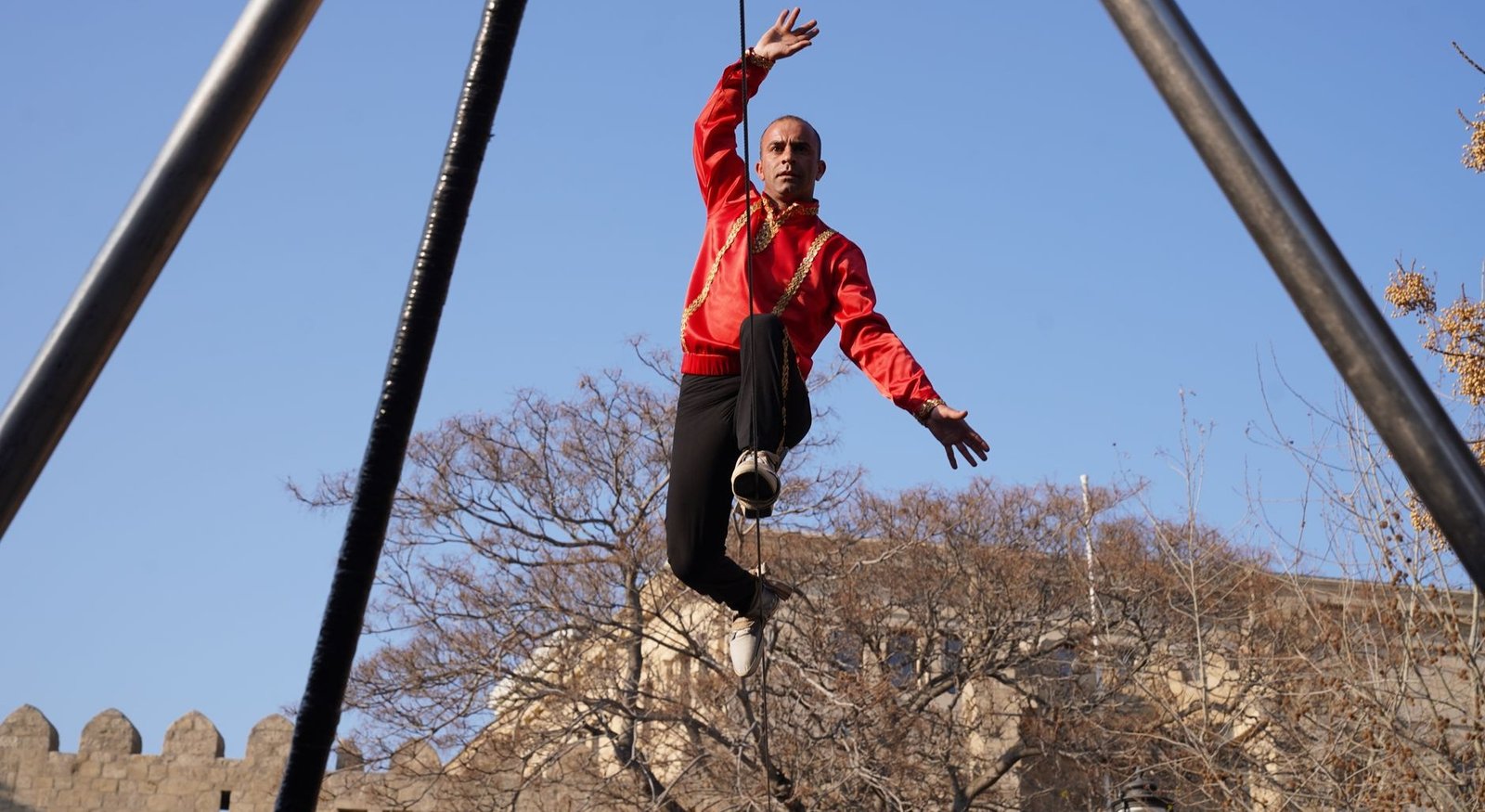 Paris Quartier d'Été 2026: Dança, Teatro e Circo Gratuitos ao Ar Livre (Guia Completo) 2 Artista acrobata em fantasia vermelha equilibrando em corda ao ar livre contra céu azul de Paris