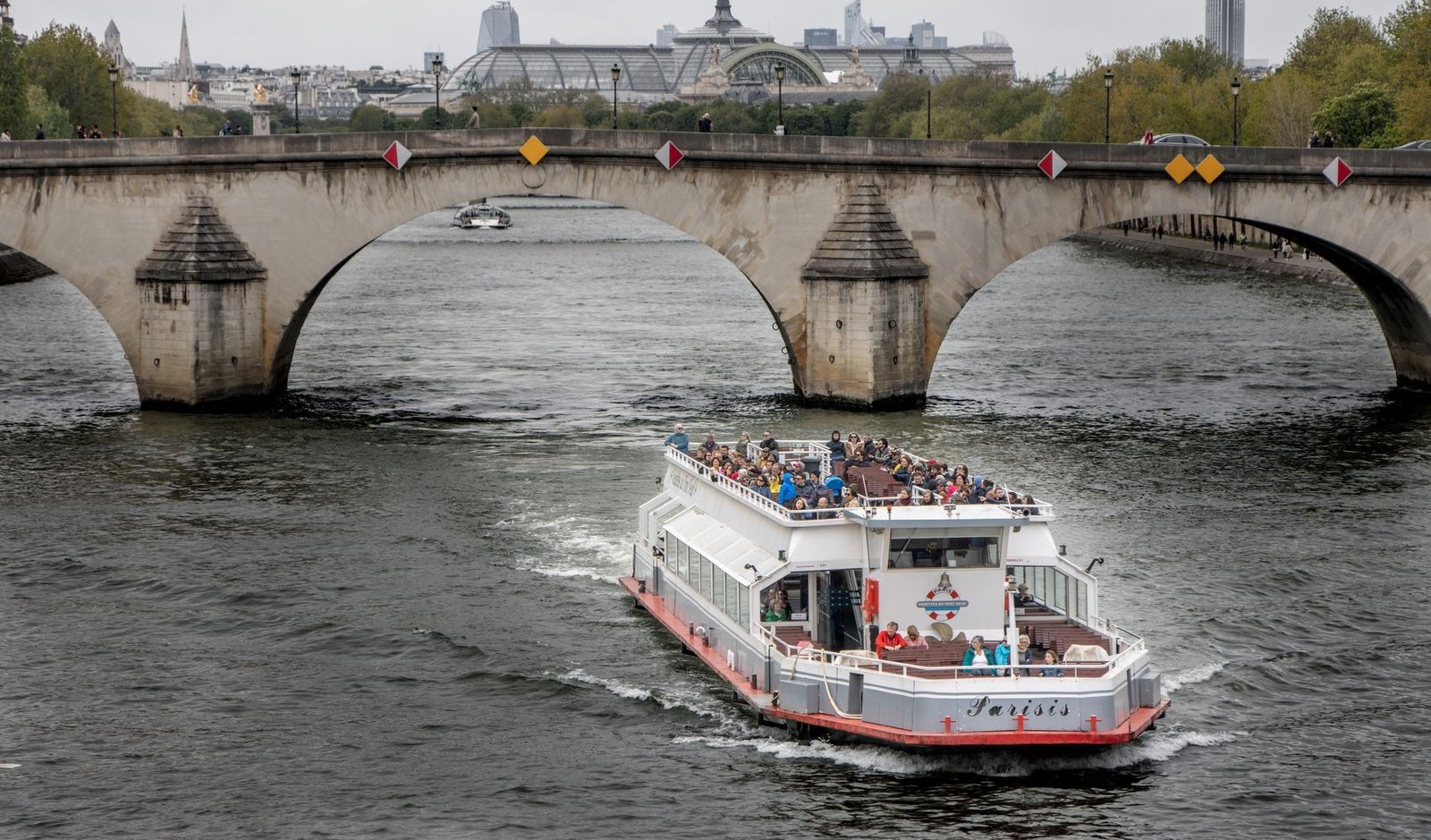 Passeio de Barco no Sena: Vale a Pena Fazer? 1 Barco de turismo passando sob uma ponte histórica no Rio Sena em Paris