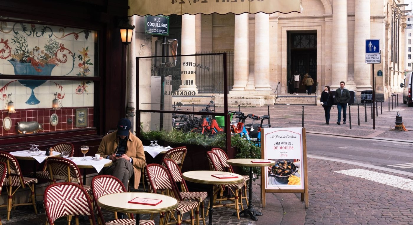 HOME 2 Café parisiense com mesas na calçada e arquitetura histórica ao fundo