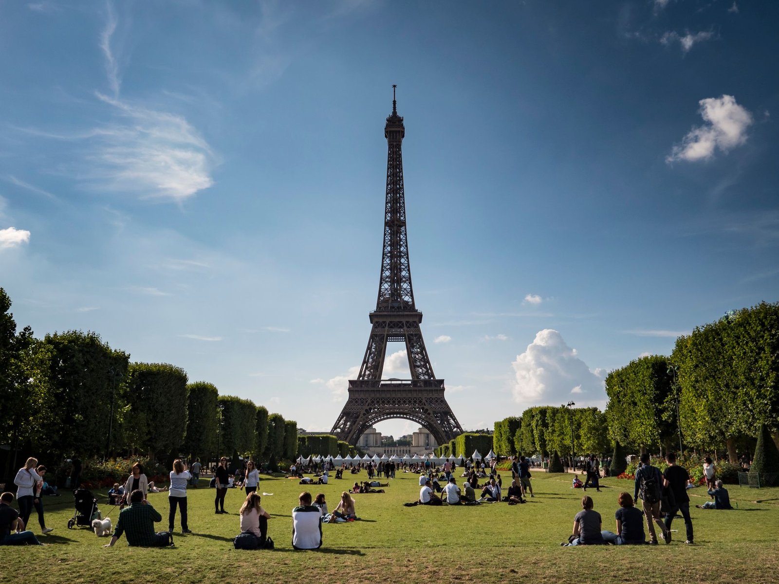 Torre Eiffel com Crianças: Guia Completo para Famílias 2 Pessoas sentadas no gramado em frente à Torre Eiffel