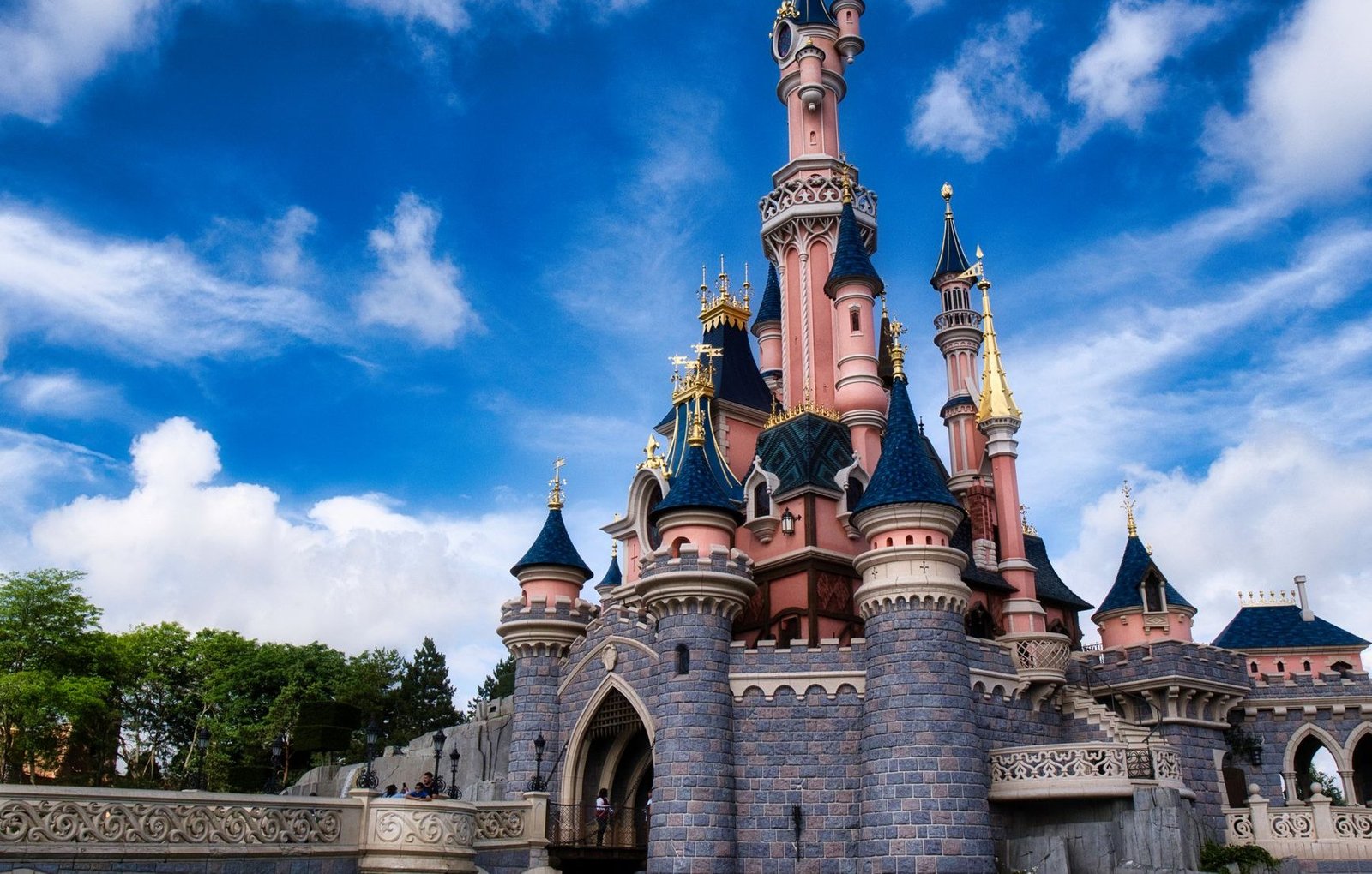 HOME 2 Castelo da Bela Adormecida iluminado no Disneyland Paris sob céu azul com visitantes na frente