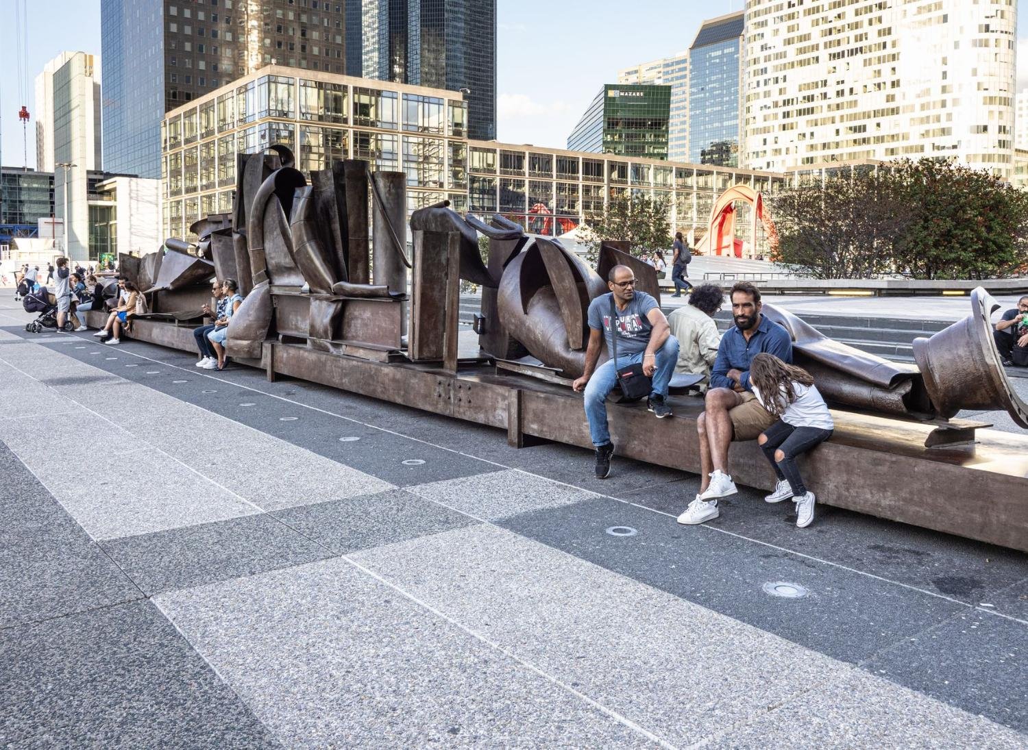 La Défense: o Bairro Moderno e Futurista de Paris 3 Pessoas descansam perto de escultura moderna na esplanade de La Défense em Paris