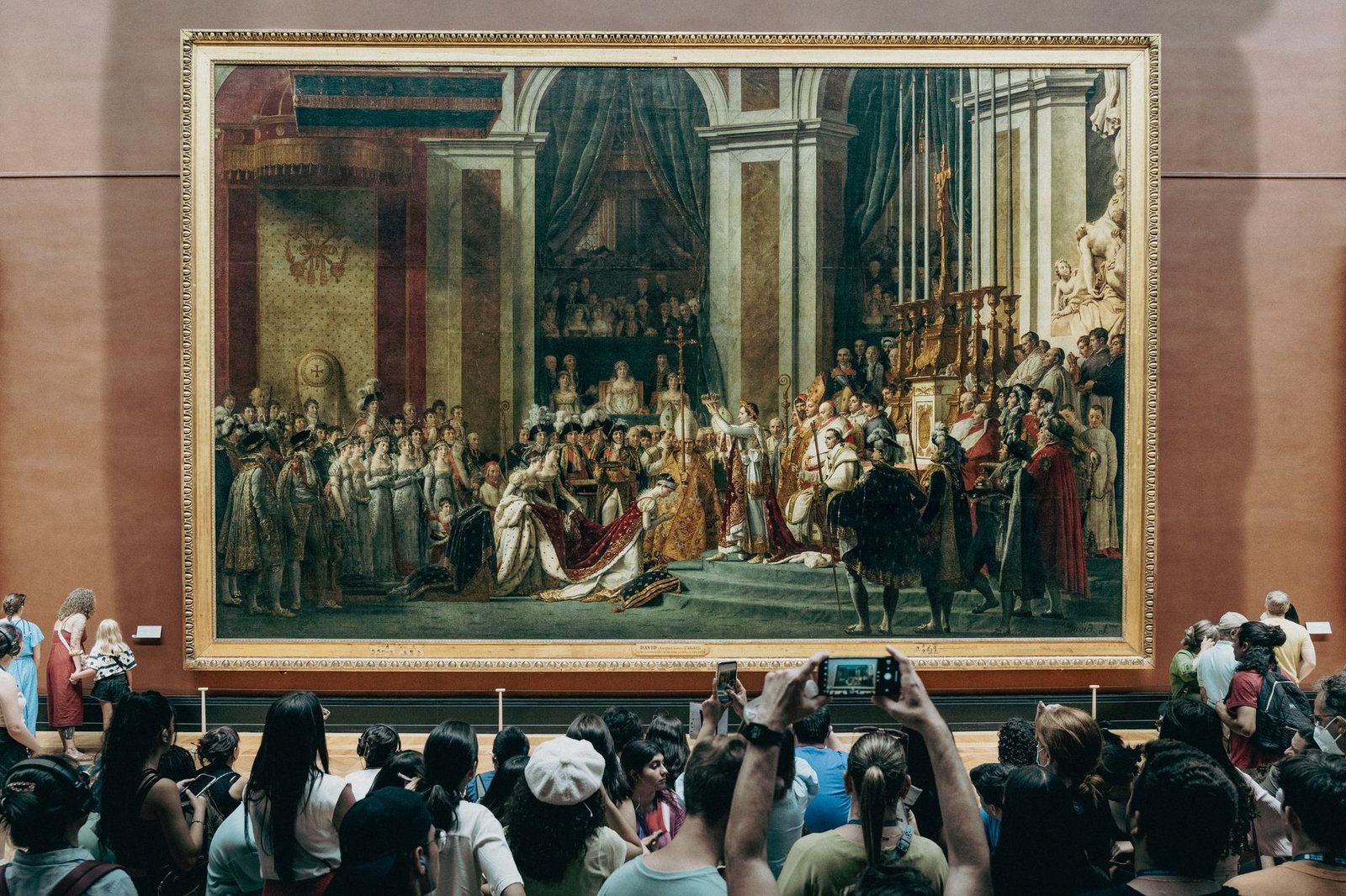 Como Encontrar a Mona Lisa no Louvre (e o Que Ninguém Te Conta Sobre Ela) 3 Visitantes fotografando grande pintura na galeria do Louvre
