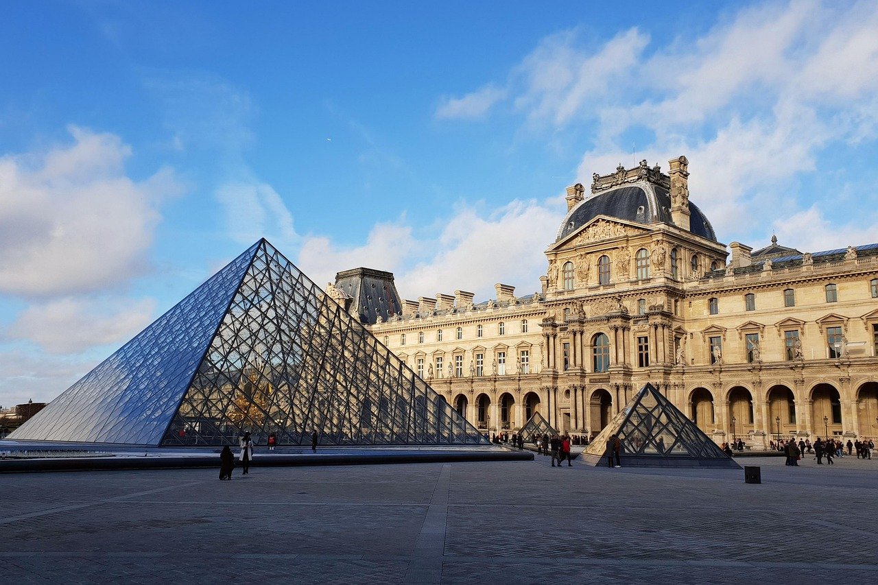 Museu do Louvre: Ingressos, Como Evitar Filas e o Que Ver 4 Pirâmide de vidro do Louvre e o palácio sob céu azul durante o dia