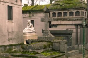 Vista de um túmulo antigo no Père Lachaise com estatua e galho de árvore
