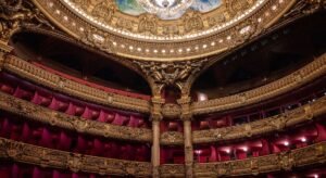 Interior luxuoso de teatro parisiense com detalhes dourados e lustre de cristal