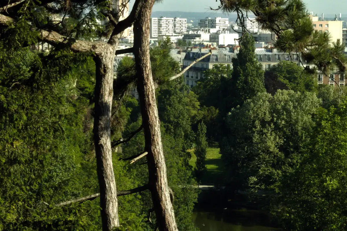 Parc des Buttes-Chaumont: o que ver mesmo com obras 2 Árvores e relevo do Parc des Buttes-Chaumont com prédios de Paris ao fundo